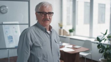 Orta boy, kendinden emin, gözlüklü, kollarını kavuşturup kameraya bakan bir adamın görüntüsü.