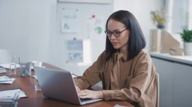 Çekici Asyalı esmerin laptopta çalışırken ve kameraya gülümserken orta boy portre görüntüleri.