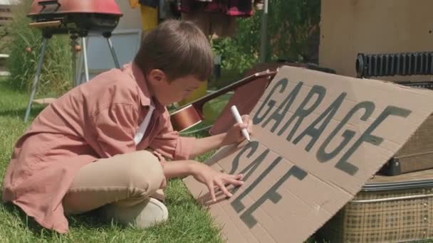 Handheld Tiro Menino Bonito Sentado Grama Verde Fazendo Sinal Papelão — Vídeo de Stock