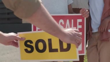  Eşi ve çocukları yanında dururken, tanınmayan adamın yavaş yavaş satılık tabelasına etiket yapıştırması.