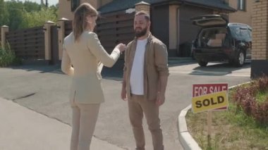  Genç bayan emlakçının mutlu sakallı bir adamın evinin anahtarlarını asıp elini sıkarken çekilmiş.