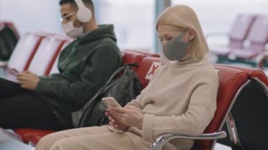 Çok ırklı, koruyucu maskeli, uçuş için bekleme salonunda bekleyen çok ırklı insanların orta yavaş bir şekilde yakın çekimi.