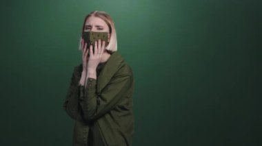 Yeşil arka planda poz veren çivili maskeli kızgın kadın modelinin portresi.