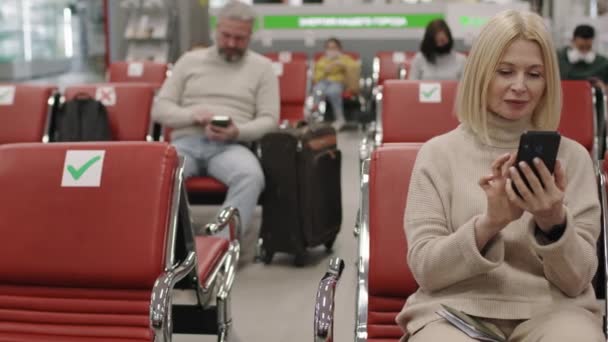 스마트폰을 사용하여 비행을 기다리는 매력적 코카서스 여성의 중간느리게 다음에는 카메라를 — 비디오