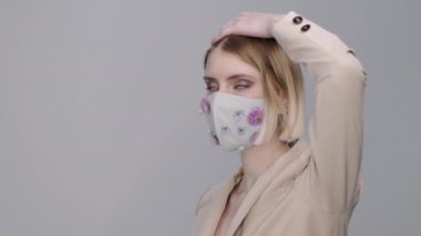 Gri arka planda duran çiçeklerle süslenmiş maskeli güzel bir genç kadının portresi.