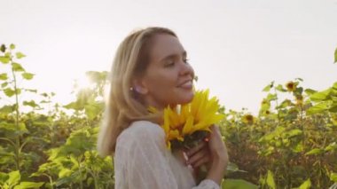 Yazlık elbiseli, elinde ayçiçeği olan, kırsal alanda kameraya poz veren güzel bir kızın yavaş çekimleri.
