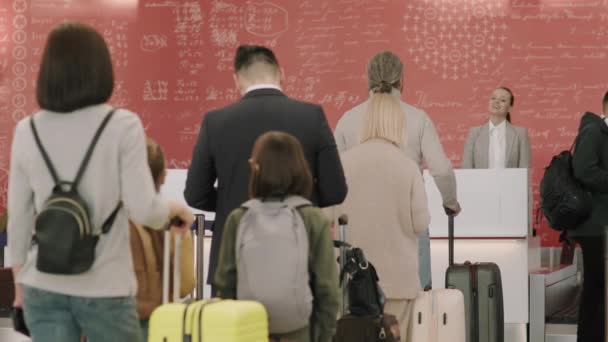 女性サービスエージェントがパスポートと手荷物を制服でチェックしながら 列に並んでチェックインカウンターに立つ乗客の中バックビュー映像 — ストック動画