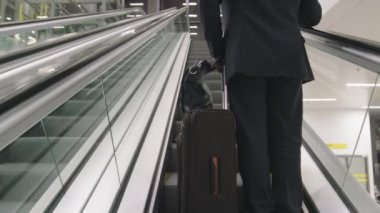 Coronavirus sırasında havaalanındaki yürüyen merdivende bavulunu kaldıran iş adamının yavaş çekimde arka plan görüntüsü.