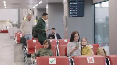 Yavaş çekimde, havaalanındaki dinlenme odasında yolcu bekleyen insanların orta ölçekli görüntüleri.