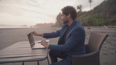 Akıllı erkek serbest bilgisayarın işini bitirdiği, sahil şeridindeki pembe günbatımının keyfini çıkardığı orta ölçekli bir kare.