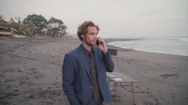 Beyaz elbiseli beyaz iş adamının tropik bölgelerde boş kıyı şeridi boyunca yürürken telefonla konuştuğu görüntülerin izini sürüyorum.