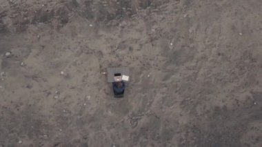 Üst görüntüde, iş adamı gibi yalnız başına oturmuş, ıssız bir plajda dizüstü bilgisayarla uğraşan birinin görüntüsü var.