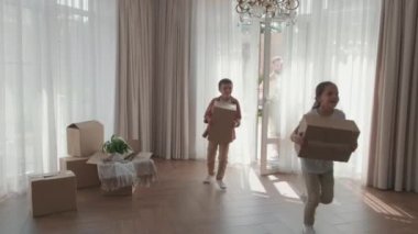  Yeni evlerine karton kutularla koşan heyecanlı küçük çocukların el kamerasıyla çekilmiş görüntüleri. Oturma odasına bakarken gülümseyen ve konuşan mutlu bir adam ve kadın.