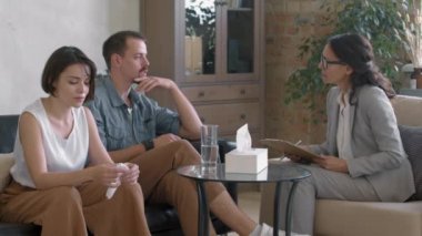 Orta yaşlı kadın psikoterapist sandalyede oturuyor ve çiftler terapisi yürütüyor.