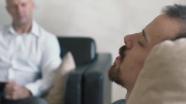 Zihinsel sorunları olan genç bir adamın yakından çekimleri. Sandalyeye uzanmış, gözleri kapalı ve erkek terapistle mücadelesini paylaşıyor.