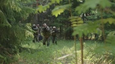 Profesyonel askeri gözetim memurlarından oluşan bir ekibin orta çaplı bir şekilde yaklaşarak yaz ormanından geçerek kameraya doğru ilerleyerek düşman var mı diye tüfek günü dürbününe bakıyorlar.