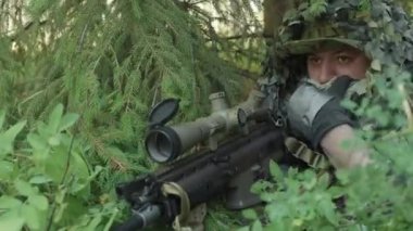 Sığınakta oturmuş, tüfekli tüfeğin dürbününe bakan ve ormandaki askeri operasyonları hedef alan orta ölçekli bir asker görüntüsü.