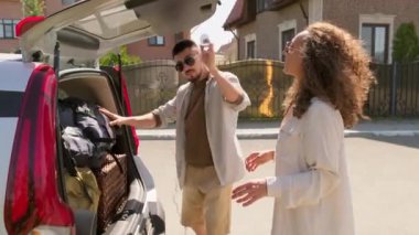 Maceracı genç adam ve kadın valizlerini bagaja koyup yolculuk hazırlıklarını tamamlıyor ve beşlik çakıyor.