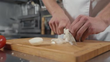 Lokanta mutfağında ahşap kesim tahtasıyla soğan kesen tanınmayan bir erkek aşçının yavaş çekimde yakın çekimi.