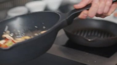 Çok renkli sebzeleri kızartırken tavayı tutan tanınmayan bir aşçı elinin yavaş çekimde yaklaşması.