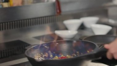 Tanınmayan şefin, sebzeleri ateşte kızartıp, ticari mutfakta tavaya atması.