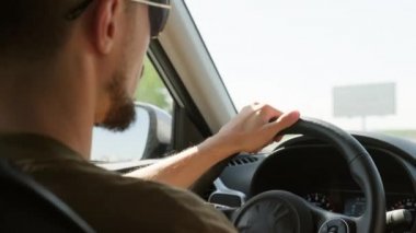 Omuzlarından güneş gözlüklü, tanınmayan bir adamın araba sürerken ve biriyle sohbet ederken çekilmiş fotoğrafı.