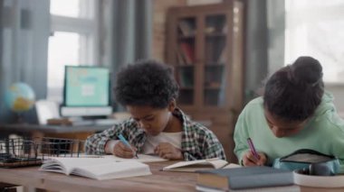Masada oturup ders çalışan birkaç tatlı afro çocuğun orta yavaş çekim görüntüsü.