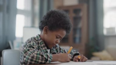 Modern oturma odasındaki masada otururken küçük afro çocuğun çizimlerini yavaş çekimde çekiyorum.