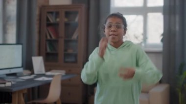 Evde kameraya bakarak müzik eşliğinde dans eden 10 yaşındaki enerjik afro kızın orta yavaş çekim görüntüleri.