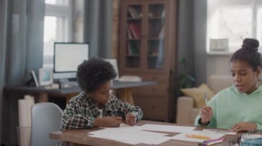 Oturma odasındaki masada oturan şirin afro kardeşlerin sohbet ederken orta ölçekli görüntüsü.