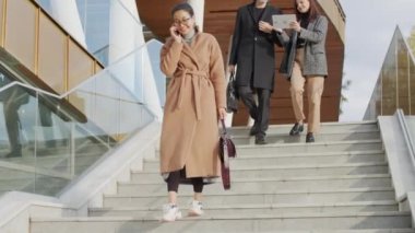 Çağdaş ofis binasından öğleden sonra merdivenlerden inen bir grup çok ırklı meslektaşın düşük açılı yavaş çekim görüntüleri.