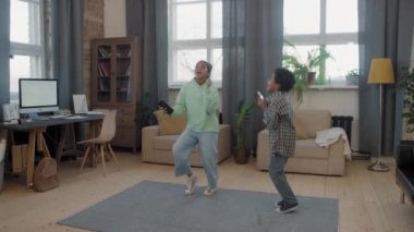 Neşeli, enerjik afro çocukların oturma odasında müzik eşliğinde dans etmesi, kızın taşınabilir hoparlörü tutması ve çocuğun akıllı telefondan video kaydetmesi.