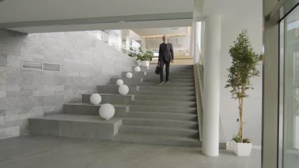 身着黑色西服的成熟的高加索商人慢吞吞地走下楼去 下班后离开现代办公大楼 — 图库视频影像