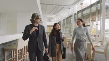 Beyazlar içinde panoramik pencereli, bej renkler içinde lüks bir restoranda yürürken çok ırklı iş adamı gibi konuşan bir grup insanın orta ölçekli yavaş çekim görüntüleri.