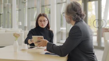 Birkaç başarılı iş ortağının birlikte restoran masasında oturup iş tartışırken ve dijital tablete bakarken orta ölçekli yavaş çekim.
