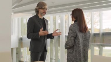 Modern ofis binasının korkuluklarında duran bayan meslektaşıyla el sıkışırken gülümseyen başarılı kıdemli iş adamının orta derece eğik videosu.