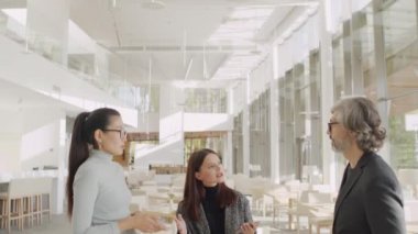 Çok ırklı meslektaşların modern restoranda panoramik pencereli durmaktan bahsederken orta-yavaş çekim çekimleri