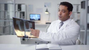 Olgun Orta Doğulu pulmonoloğun röntgen fotoğrafını internetteki toplantı sırasında kameraya çekerken orta boy portresi.