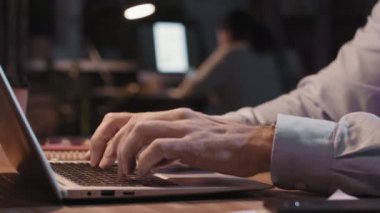 Geceleyin çatı katında dizüstü bilgisayarda yazan tanınmayan erkek elleri yavaş çekimde yakalıyor.