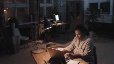 Afrika kökenli Amerikalı bir kadının bilgisayarda daktilo yazarken ve geceleri karanlık çatı katında tek başına çalışırken orta ölçekli bir yavaş çekim.