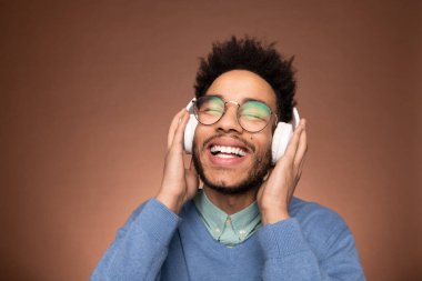 Neşeli, genç, melez bir iş adamı, kameranın önünde kulaklıkla hoş müziğin tadını çıkarırken gözlerini kapalı tutuyor.