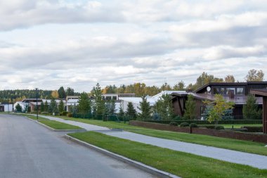 Çağdaş kır evleri ya da kırsal kesimdeki kır evleri yeşil çimenli ağaçların arasında duruyor ve önünde yol var.