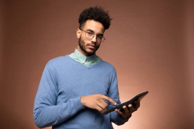 Gözlüklü genç ve ciddi bir melez işadamı kameranın önünde durup hesap makinesinin tuşlarına basarken sana bakıyor.