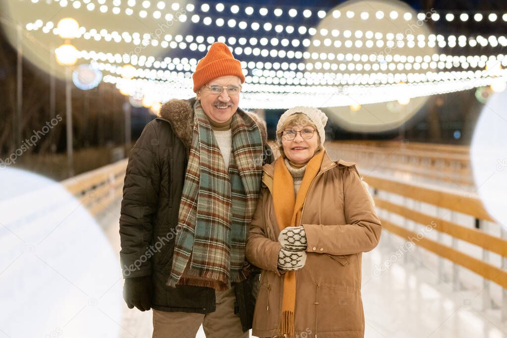 Portrait of mature couple in warm clothing smiling at camera while skating outdoors in the park