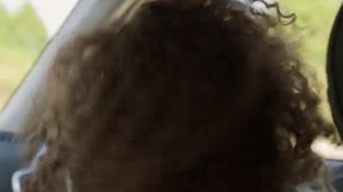 Uzun kıvırcık saçlı, müzik dinleyip arabada dans eden modern bir kadın.