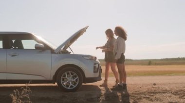 Yatay yan görüş. Yolculuk sırasında iki genç kadının araba arızasına kızdığı görüntüler.