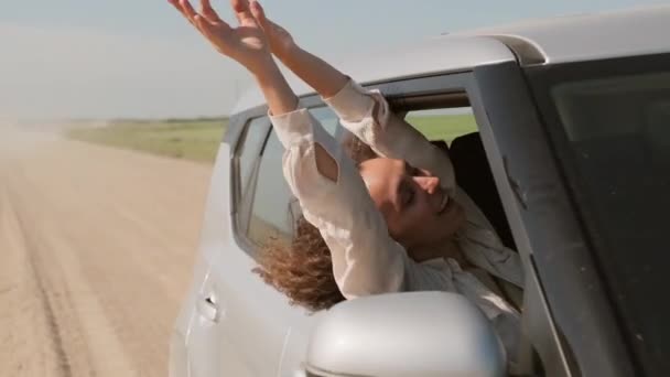 阳光明媚的夏日 一个有着一头长长的卷发的快乐的年轻女子从车窗伸出的慢镜头 — 图库视频影像