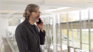 Modern binanın ikinci katında dikilirken siyah ceketli başarılı bir iş adamının telefonla konuşmasının yavaş çekim görüntüsü.