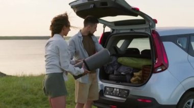 Modern Kafkasyalı genç adam ve kadın doğada vakit geçiriyorlar. Araba bagajlarını açıyorlar ve yürüyüş ve kamp için bavullarını çıkarıyorlar.