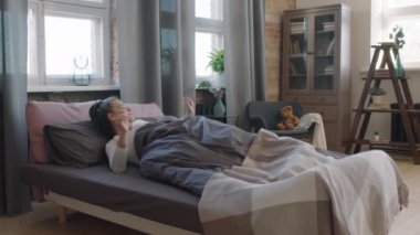 Sabahın geç saatlerinde kalktıktan sonra yatakta gerinen genç ve güzel bir kadının orta yavaş çekim görüntüleri.